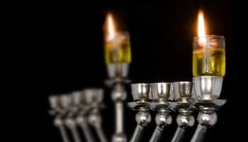 Traditional Chanukah menorah lit with olive oil, isolated on a black background; selective focus on the right flame.